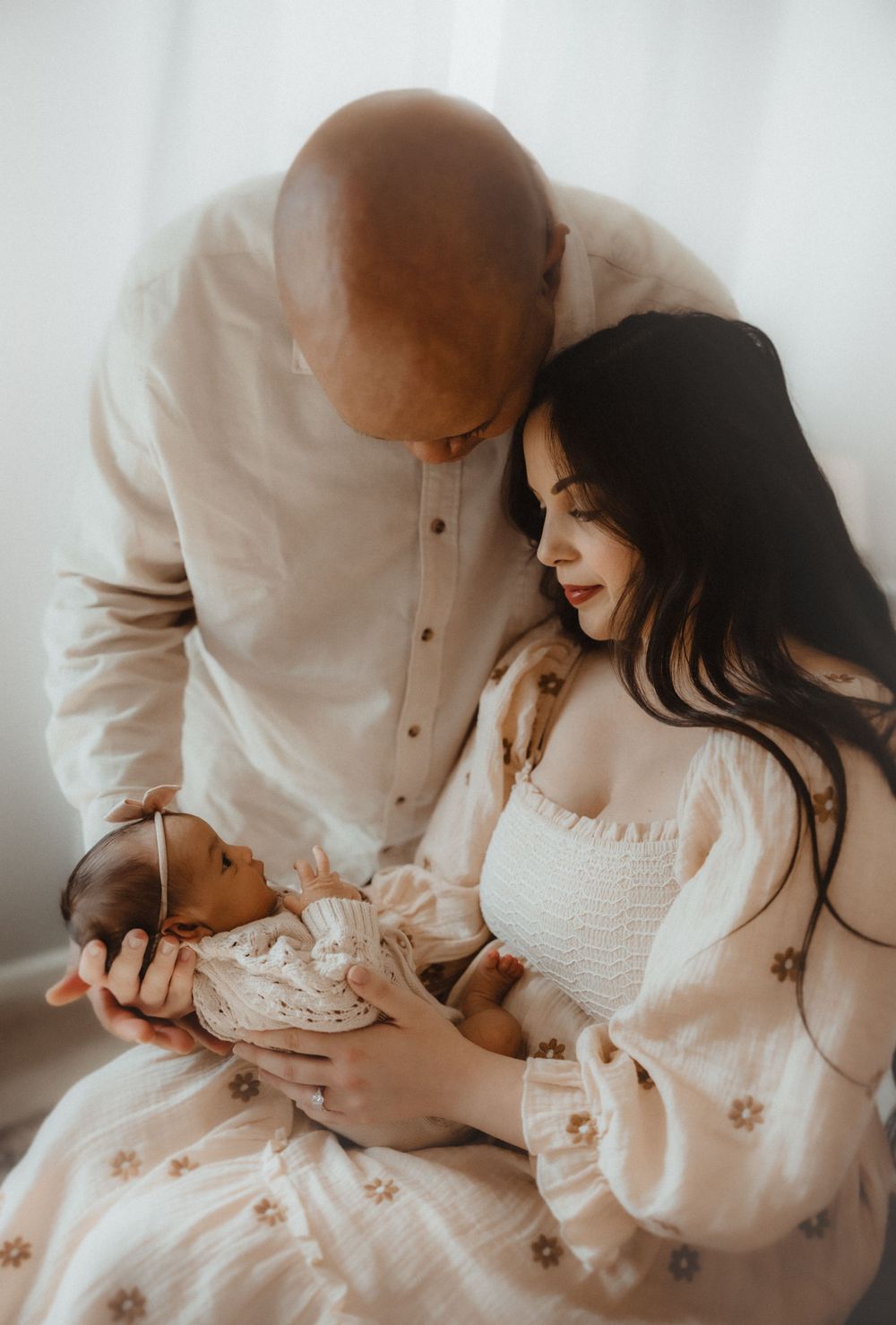 A tender family moment as parents gaze lovingly at their newborn baby in soft dreamy lighting.