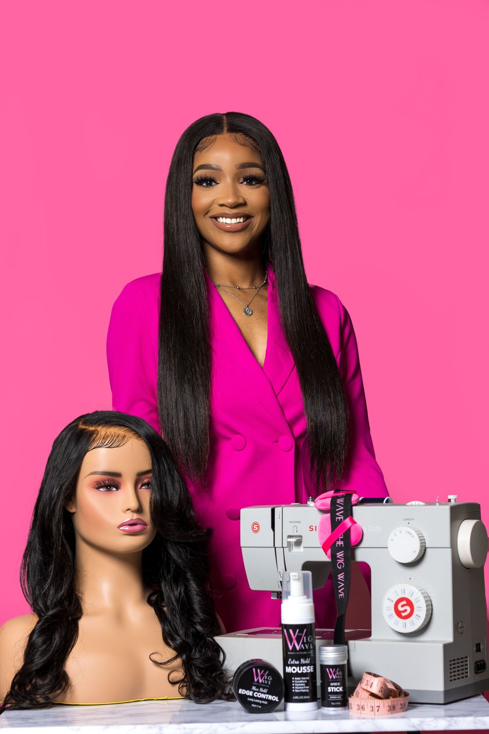 Hair stylist displays products and equipment with mannequin head against pink background.