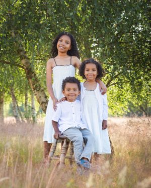 Three people in white outfits pose together against a natural background with trees.