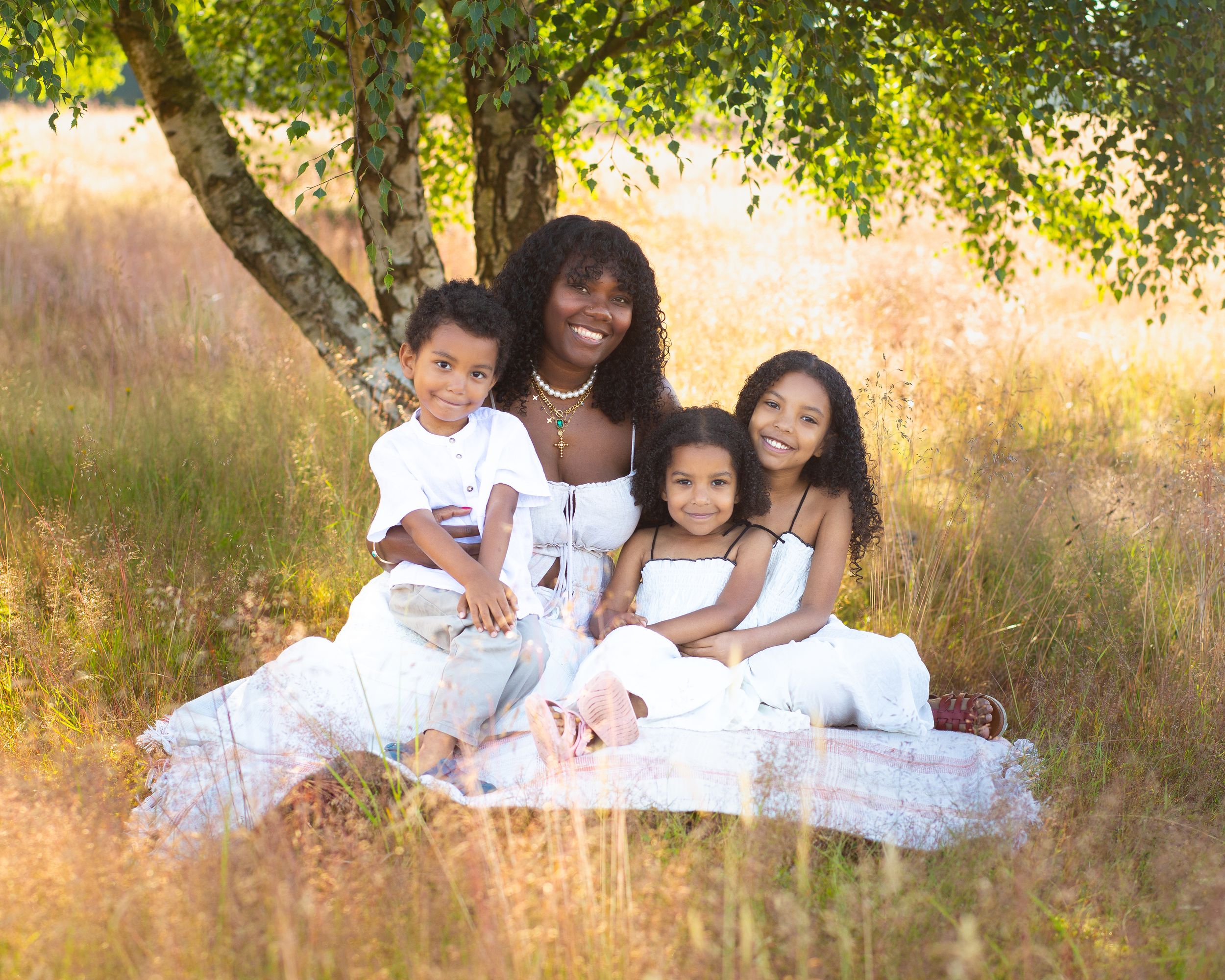A family group wearing white sits together in a sun-dappled meadow setting.