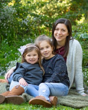 Three people sit together on a stone wall surrounded by lush green garden foliage.