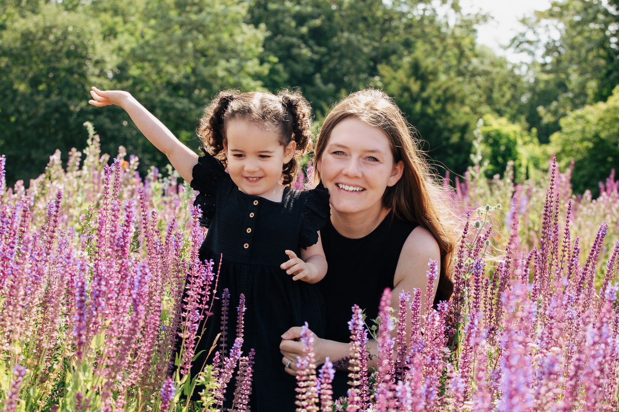 Two people pose together among purple flowering plants in a garden.