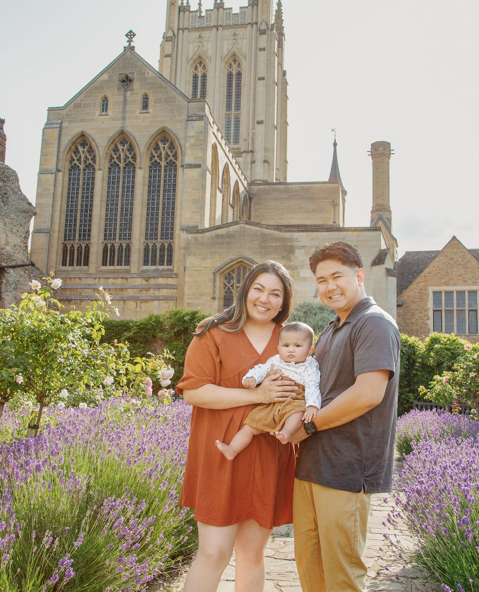 A family poses together in front of a Gothic church surrounded by lavender flowers.