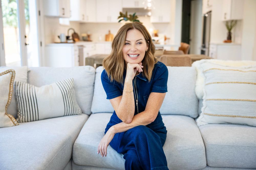Relaxed woman in navy dress sitting on light gray couch in bright modern living room with neutral decor.