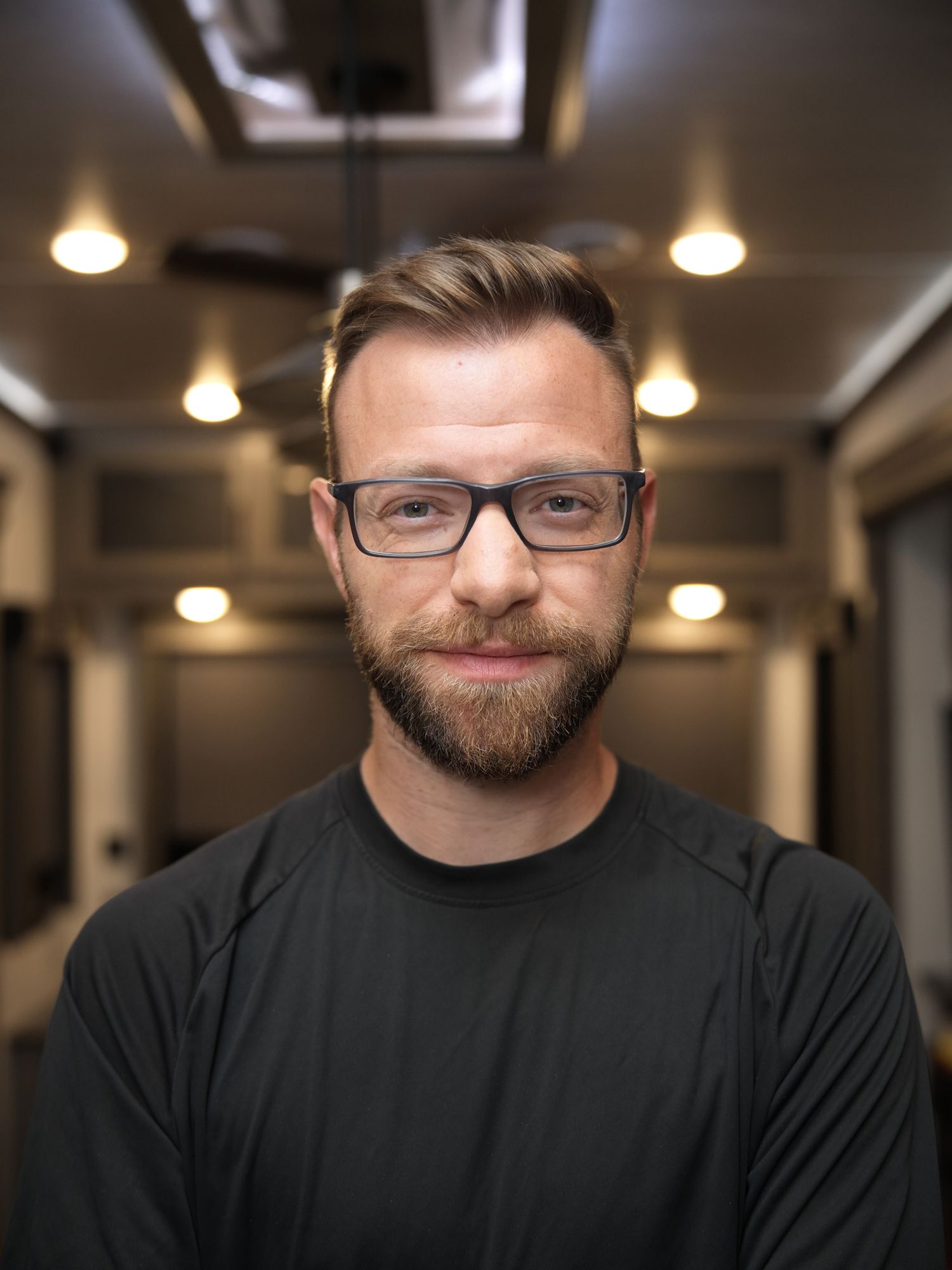 Professional headshot of a man in glasses wearing a black CARS jacket against dark background.