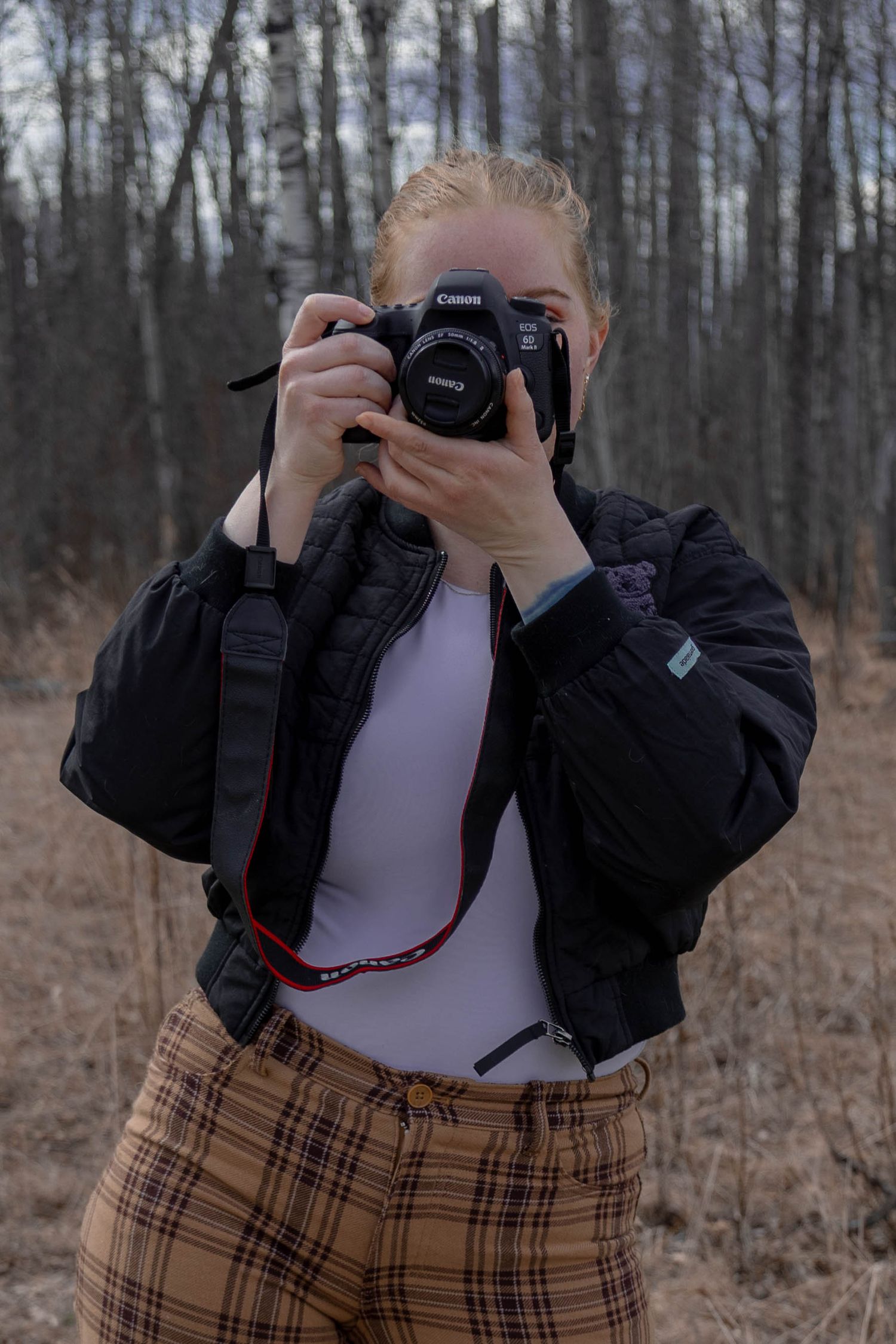 Blackboot photogrpahy's photographer holds a camera toward the photographer in a wooded area.