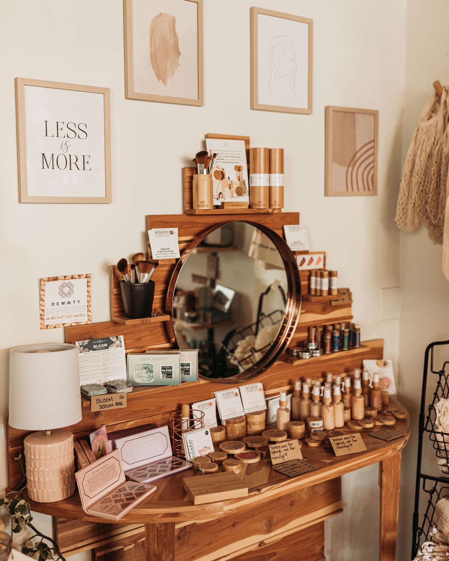 Boho-style vanity table with wooden shelves displaying makeup, skincare products, and a round mirror in warm neutral tones.