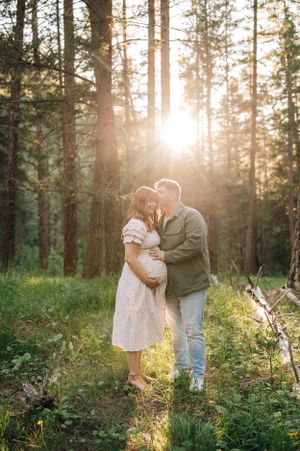 Expecting couple shares intimate moment in sunlit forest during maternity photoshoot.