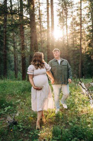 Expecting couple walking together in sunlit forest wearing casual attire.