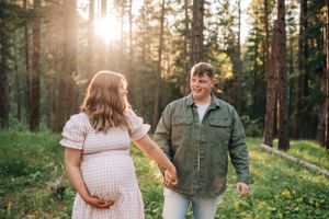 Couple shares loving glance while walking through forest during maternity session.