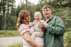 A happy family moment captured in a forest setting with a baby and parents.