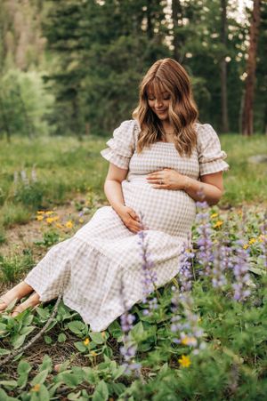A woman in a checkered dress sits among wildflowers in a forest meadow.