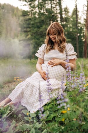 A maternity photoshoot in a forest meadow with purple wildflowers in the foreground.