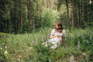 A peaceful forest scene with a woman in white dress sitting among wildflowers.
