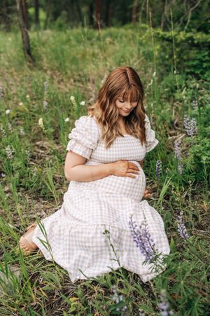 A serene maternity portrait in a forest meadow with purple and white wildflowers.