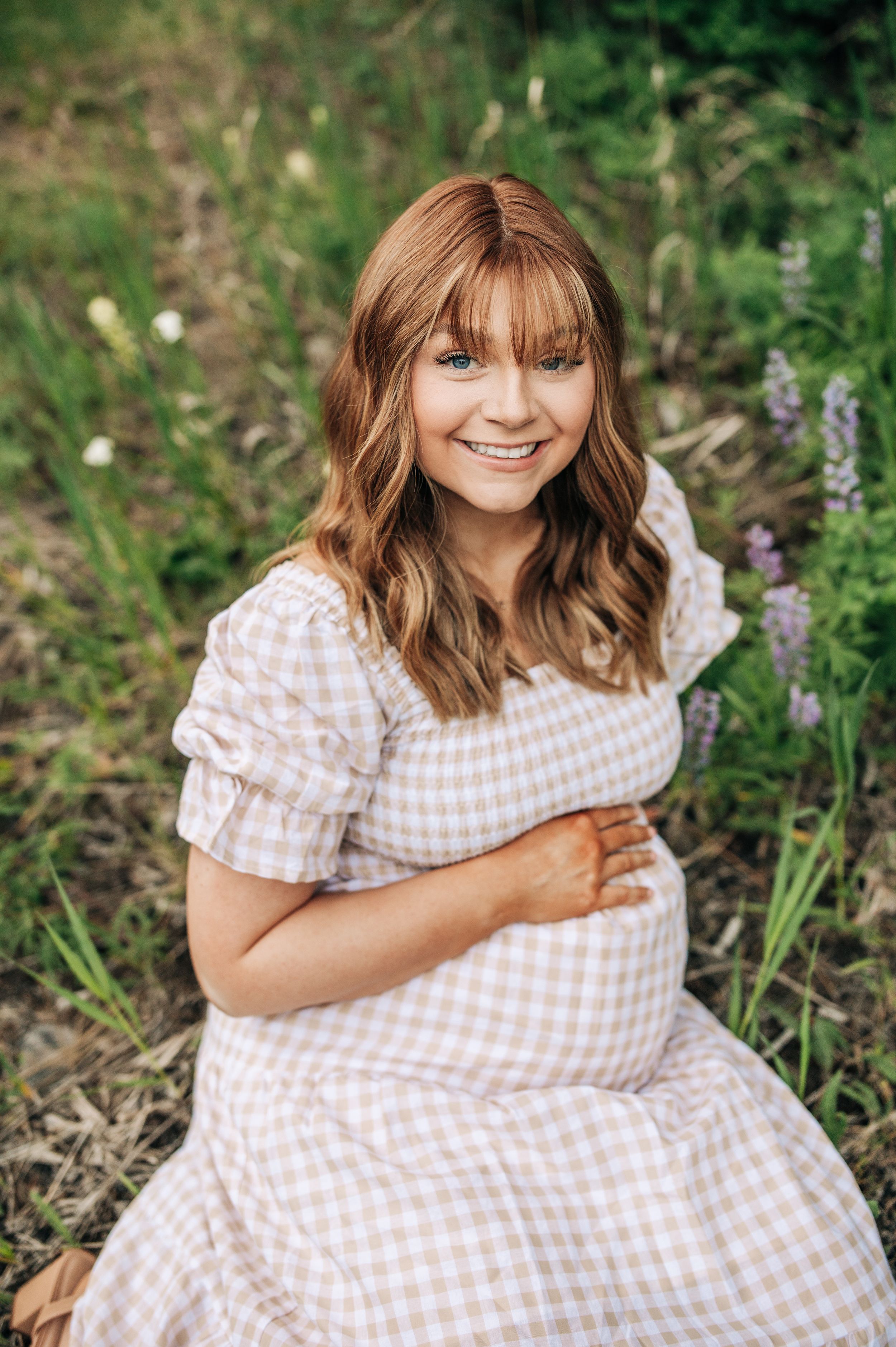 A joyful maternity portrait in a gingham dress surrounded by summer wildflowers.