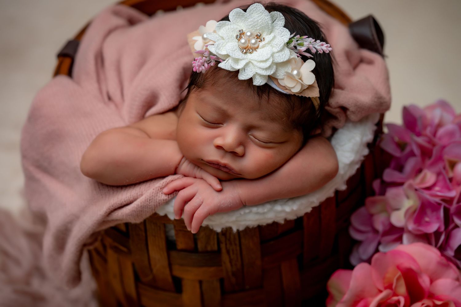 Sleeping newborn with floral headpiece surrounded by pink flowers.