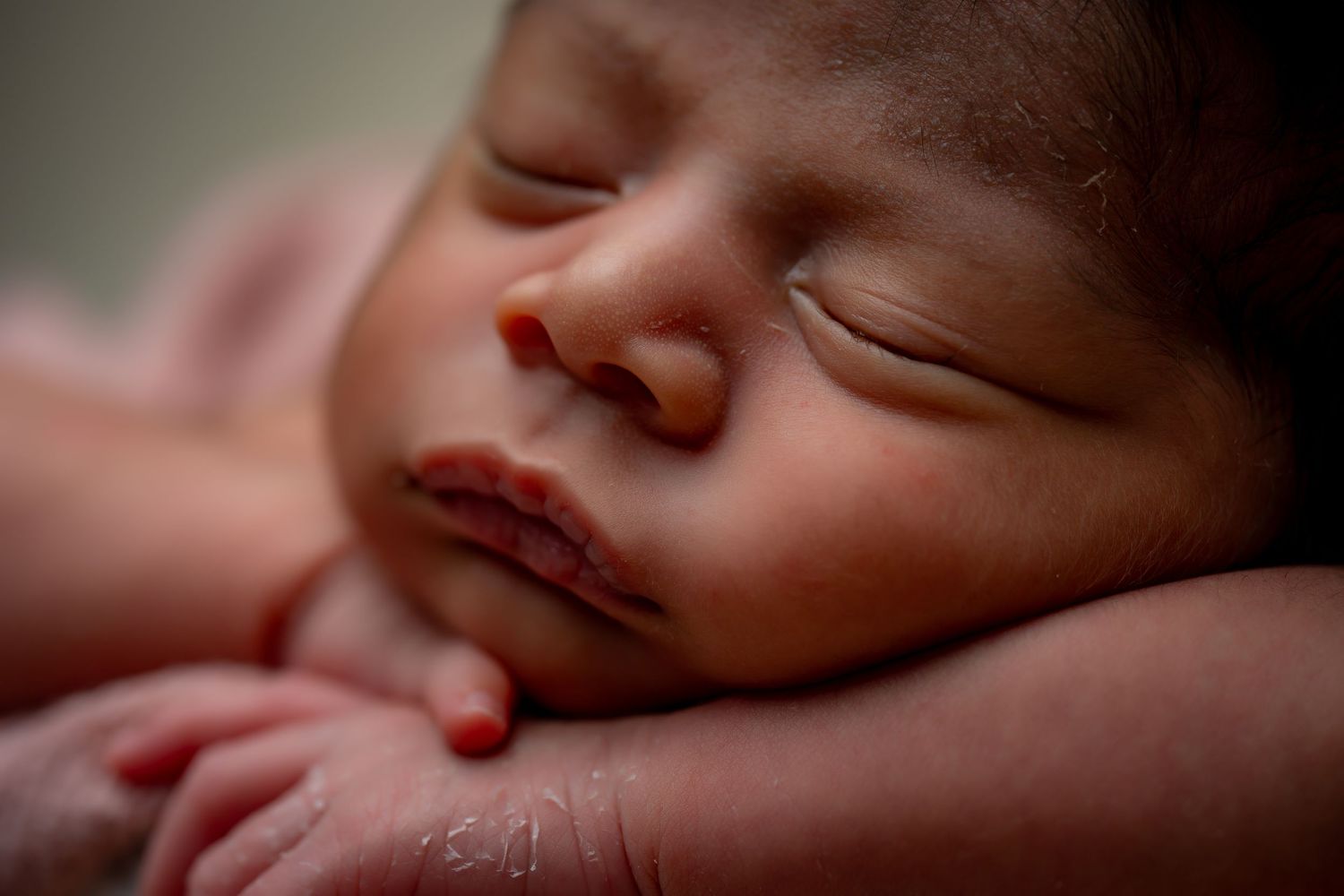 Peaceful newborn baby sleeping with a delicate white headpiece in natural lighting.