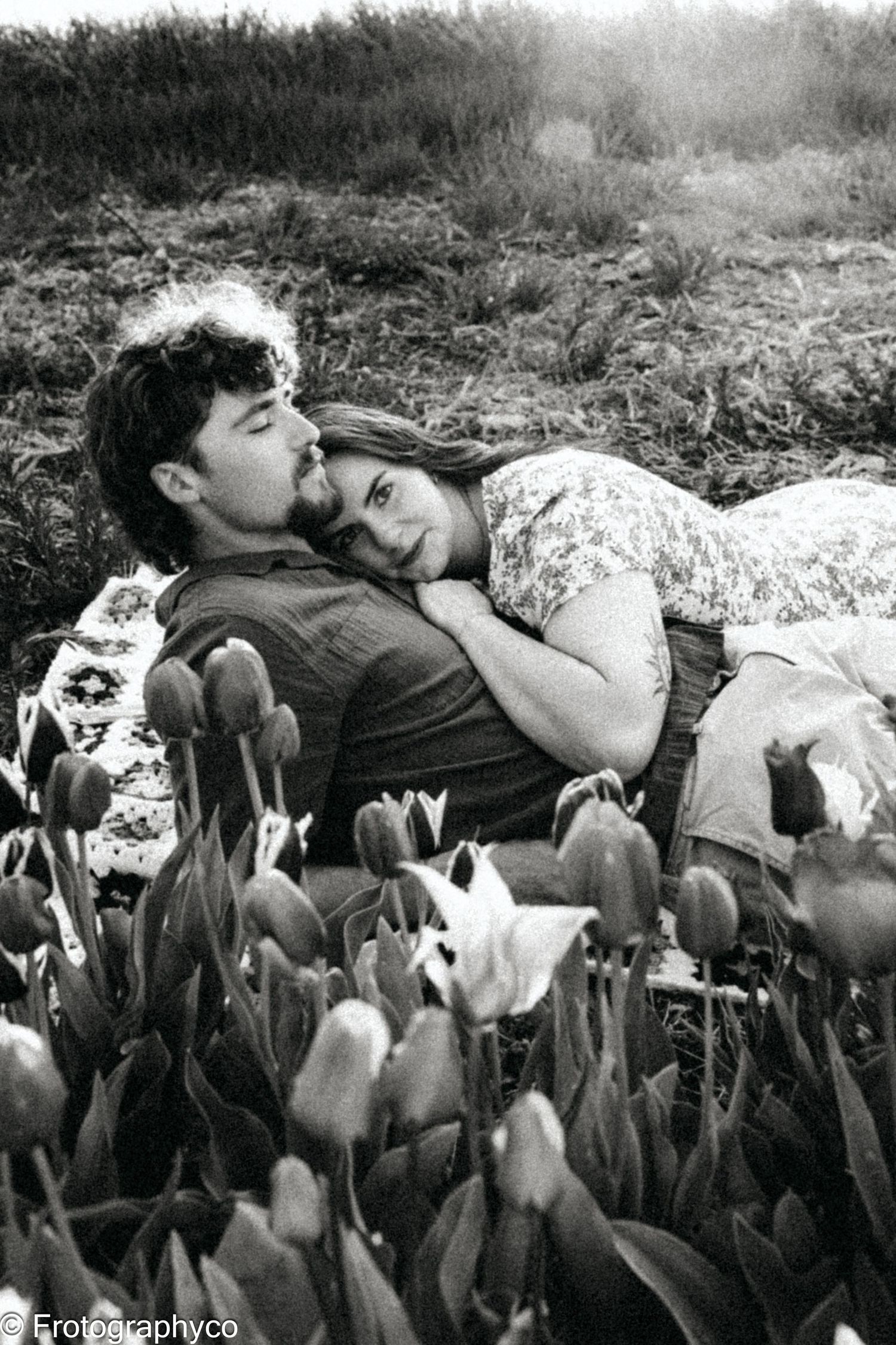 Romantic couple rests among blooming tulips in black and white photography.