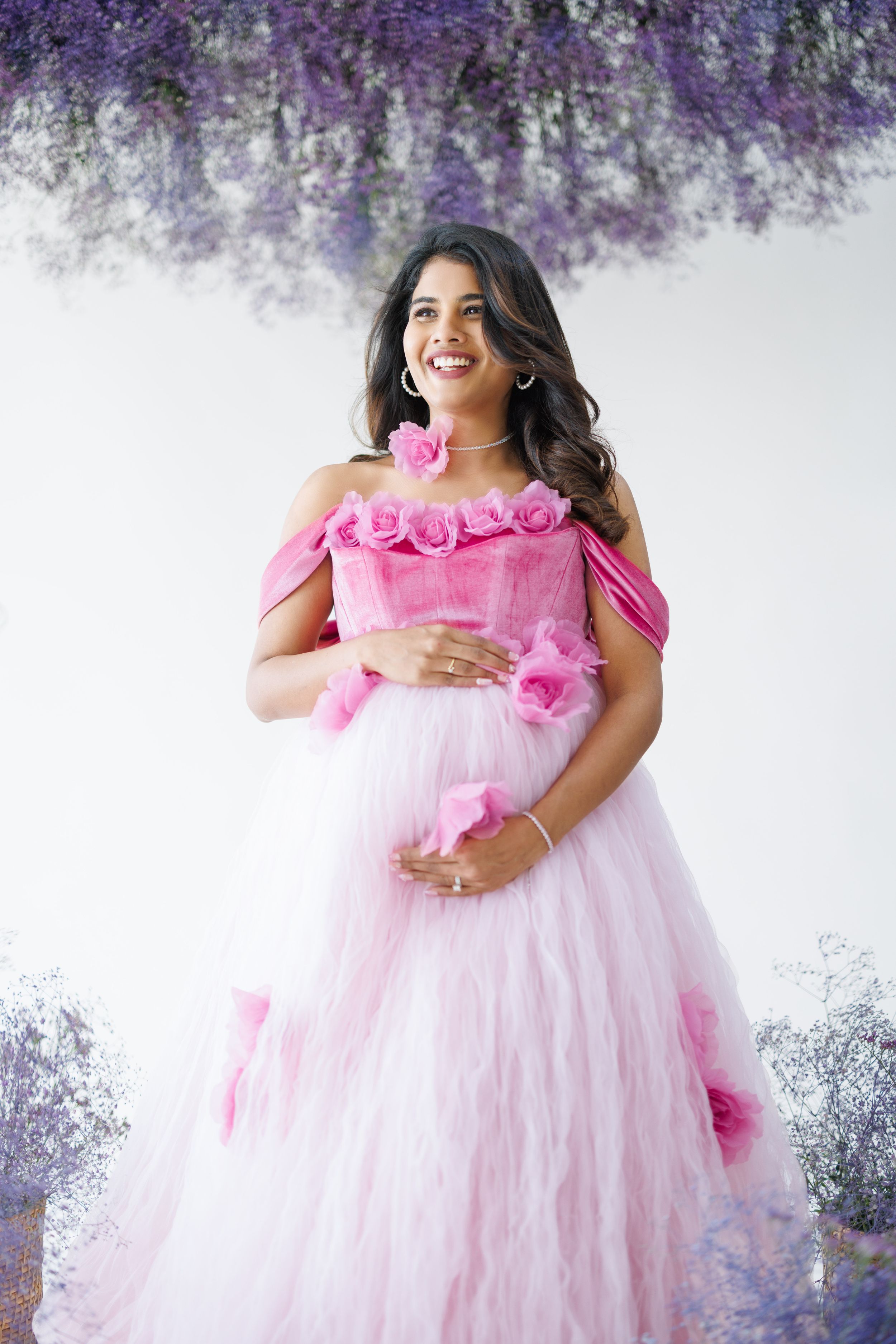 Off-shoulder pink tulle maternity dress adorned with roses against purple floral background.