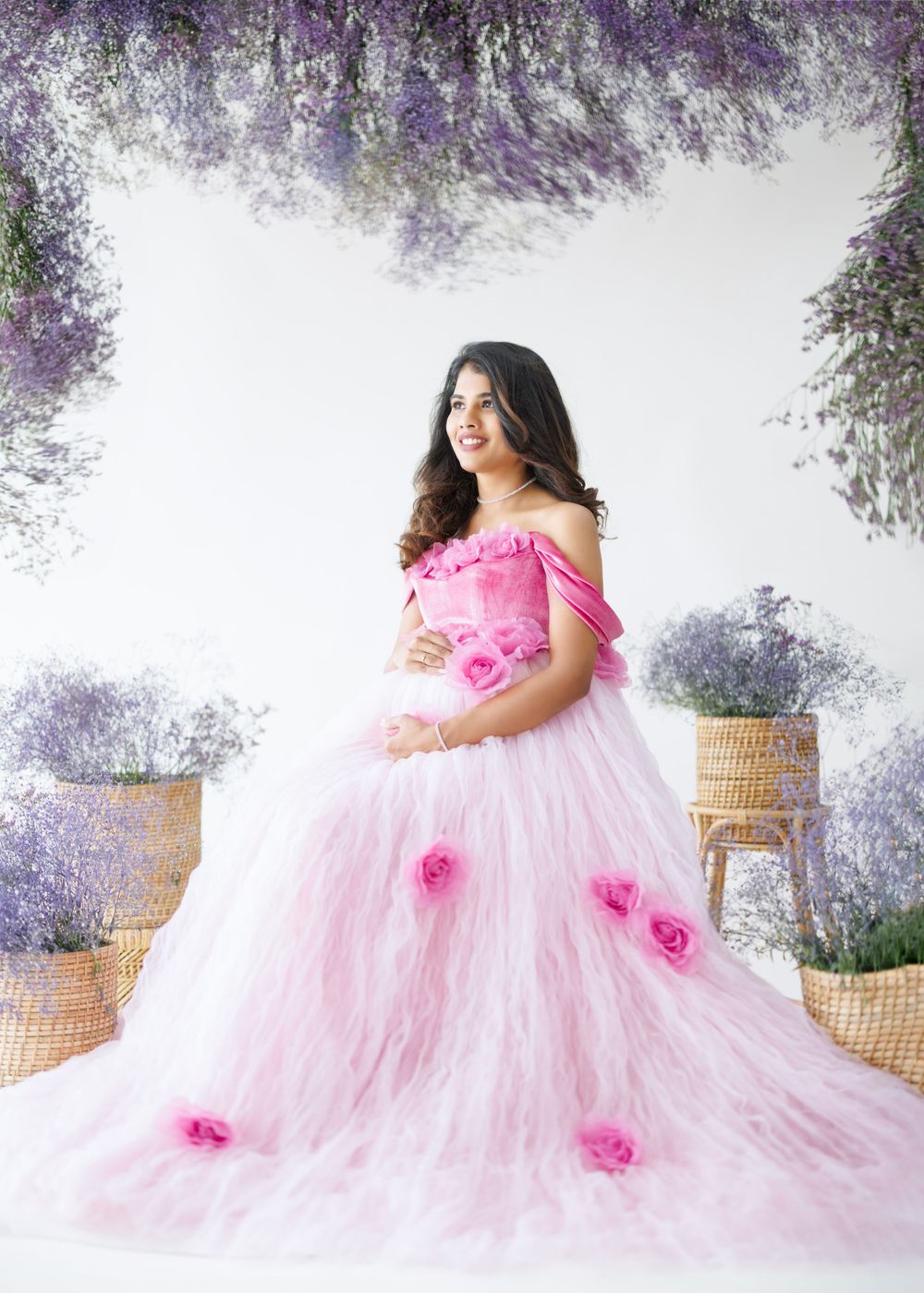 Flowing pink princess maternity gown with floral accents photographed under wisteria arch.