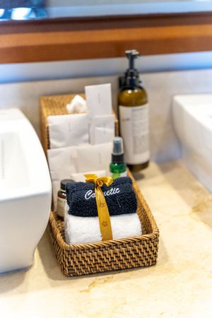 Rolled white and gray towels tied with yellow ribbon displayed in woven rattan basket next to toiletry bottles.