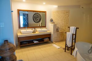 Modern spa-like bathroom interior with wooden vanity, large mirror, ceramic vessel sink and stone tile flooring.