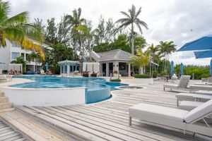 Luxury resort pool deck with lounge chairs, palm trees and white cabanas on a cloudy Caribbean day.