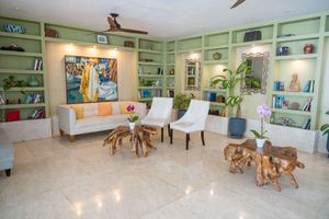 Modern waiting room with mint green built-in shelves, white chairs, and rustic wooden accent tables on polished floors.