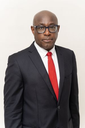 Professional headshot of someone in pinstripe suit, red tie and glasses against white background.
