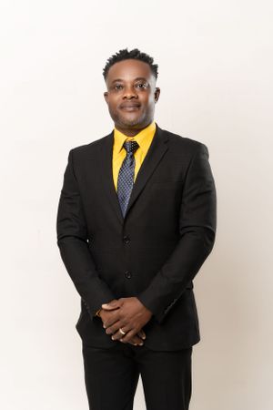 Professional portrait of person in black suit with yellow dress shirt and patterned tie.