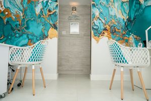 Modern waiting area with turquoise and gold marbled wallpaper and white lattice chairs on wooden legs.