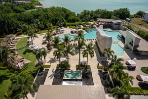 Aerial view of a luxury resort complex with multiple swimming pools, hot tubs and palm trees along a waterfront property.