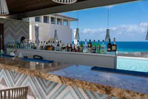 Oceanfront bar with lined up liquor bottles and geometric pattern decor overlooking a blue infinity pool and sea.