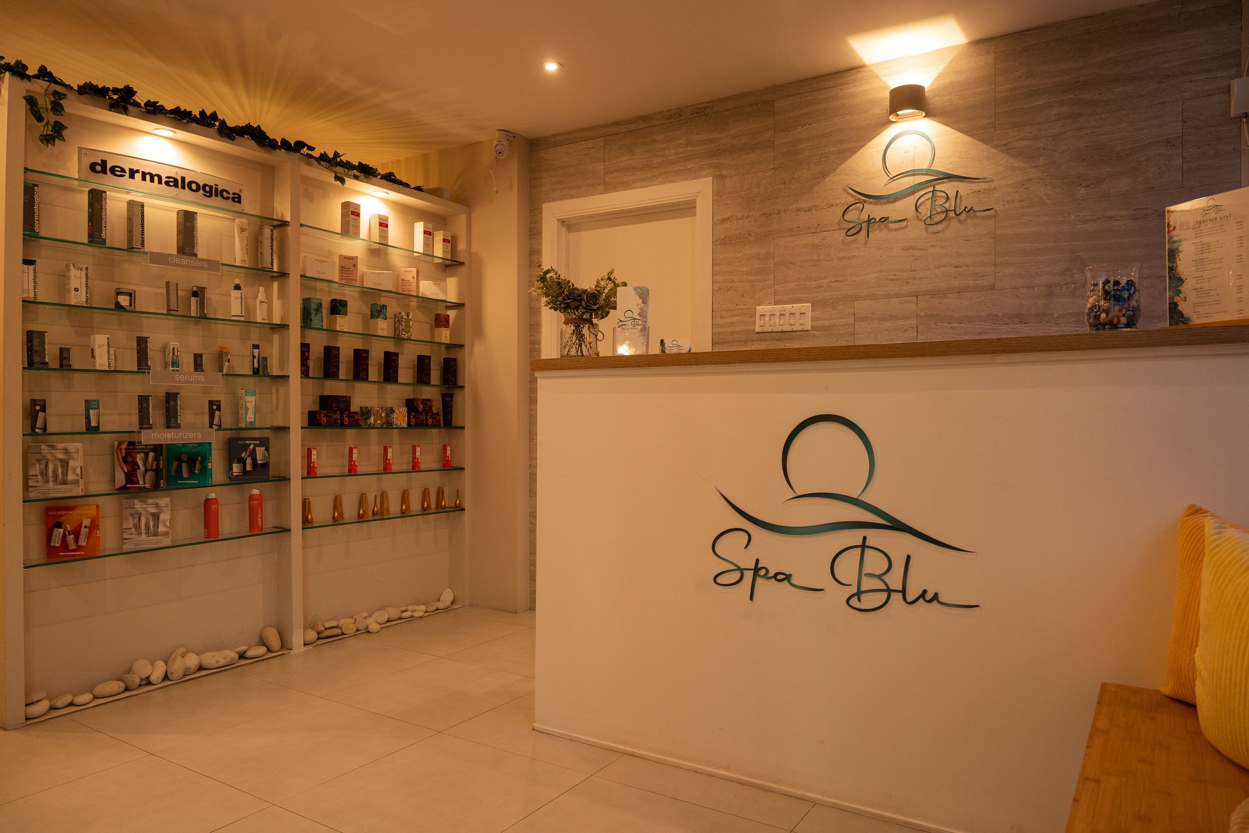 Spa reception area with illuminated product shelves and branded wall decor in warm ambient lighting.