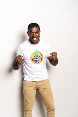 Person wearing a white t-shirt with colorful island logo and khaki pants poses energetically against white background.