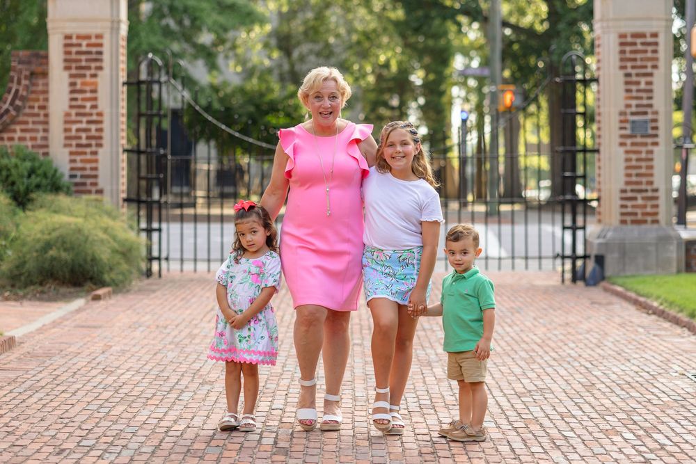 Children walk and play together on a brick pathway near ornate iron gates on a sunny day.