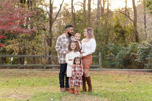A family in coordinated fall outfits poses together in a park during golden hour sunset.