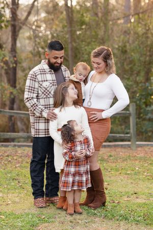 Family in coordinating plaid and white outfits share tender moments together during an autumn outdoor photo session.