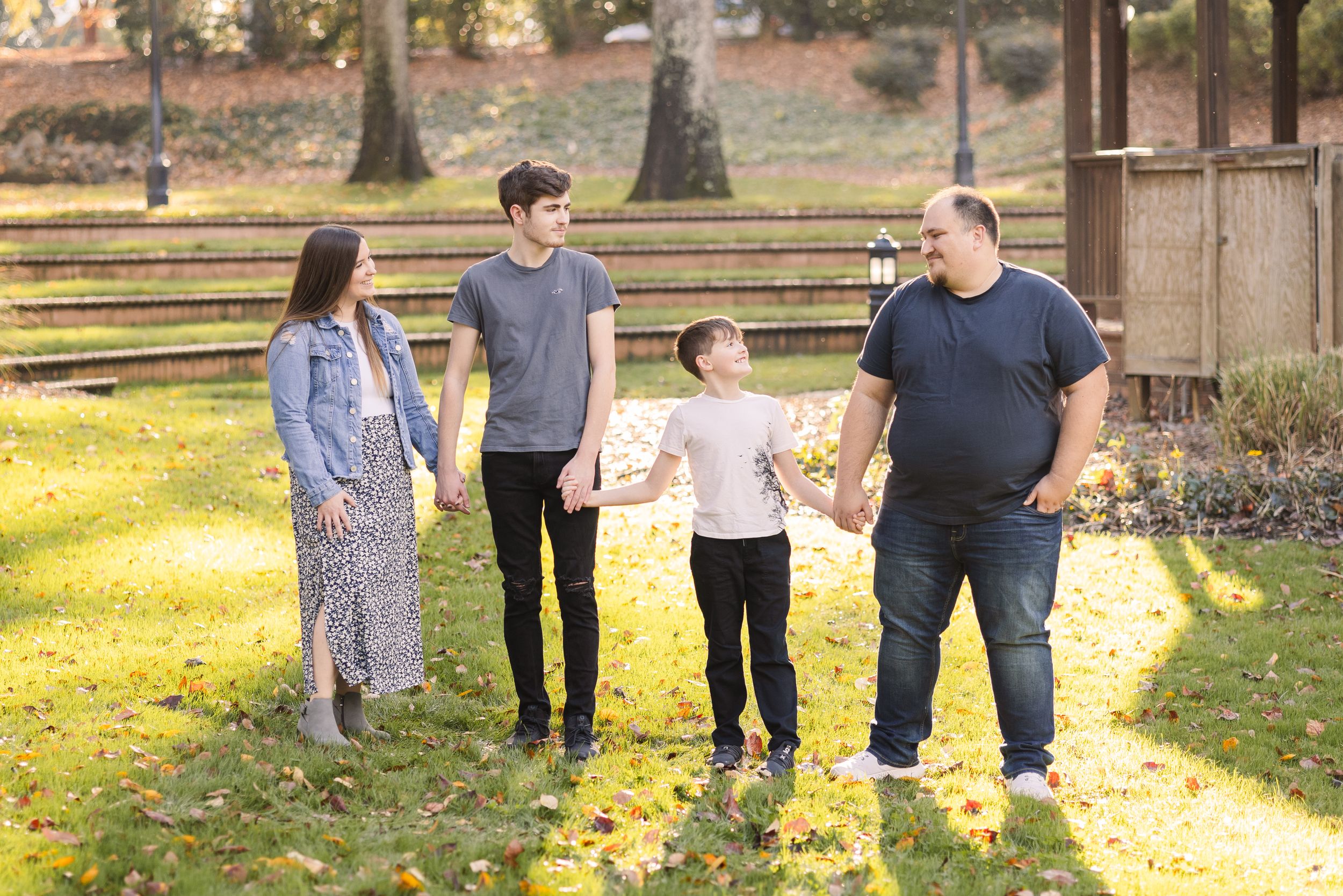 A family walks together through a scenic park during autumn with fallen leaves scattered on the ground.