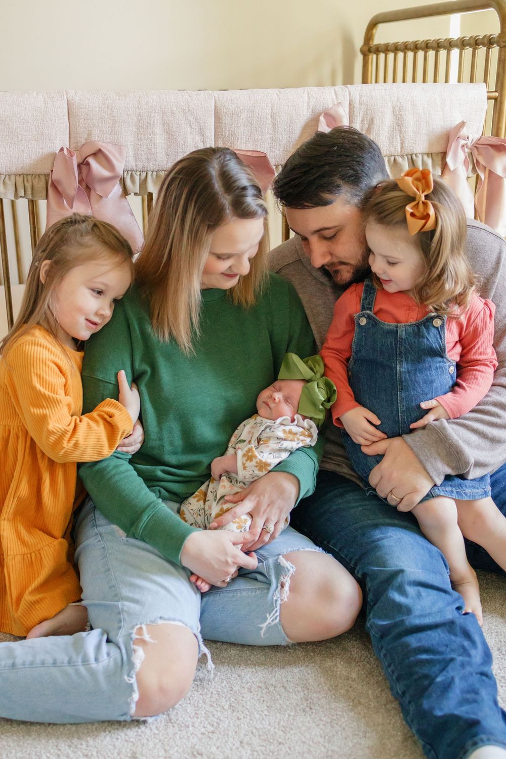 Family sitting together on couch looking down at newborn baby in tender moment.
