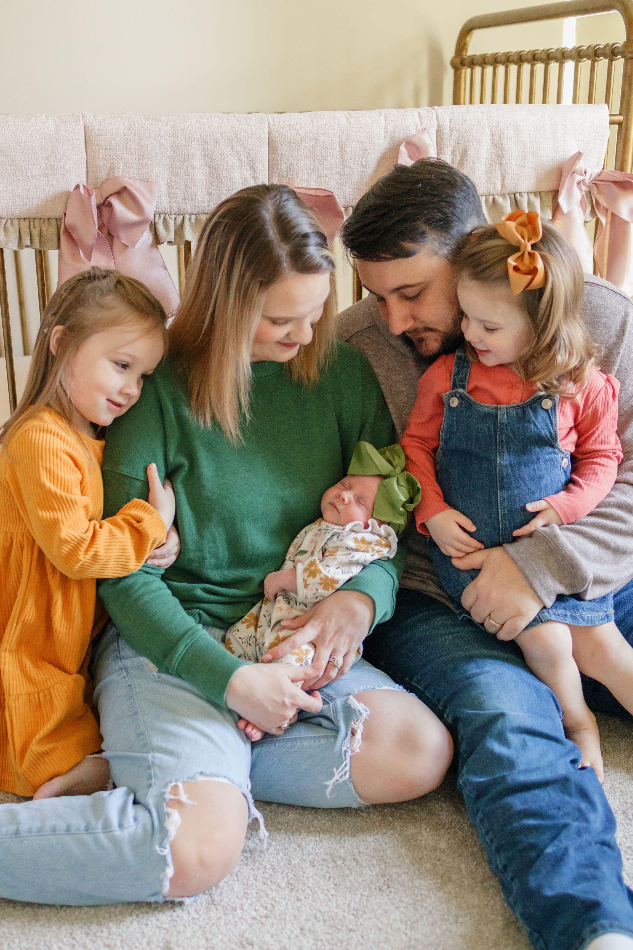 Family sitting together on couch looking down at newborn baby in tender moment.