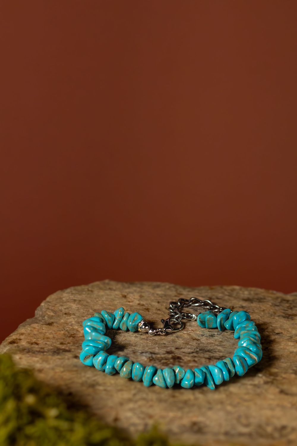 Handcrafted Native American turquoise stone bracelet with chunky beads rests on a brown rock against an earthy background.