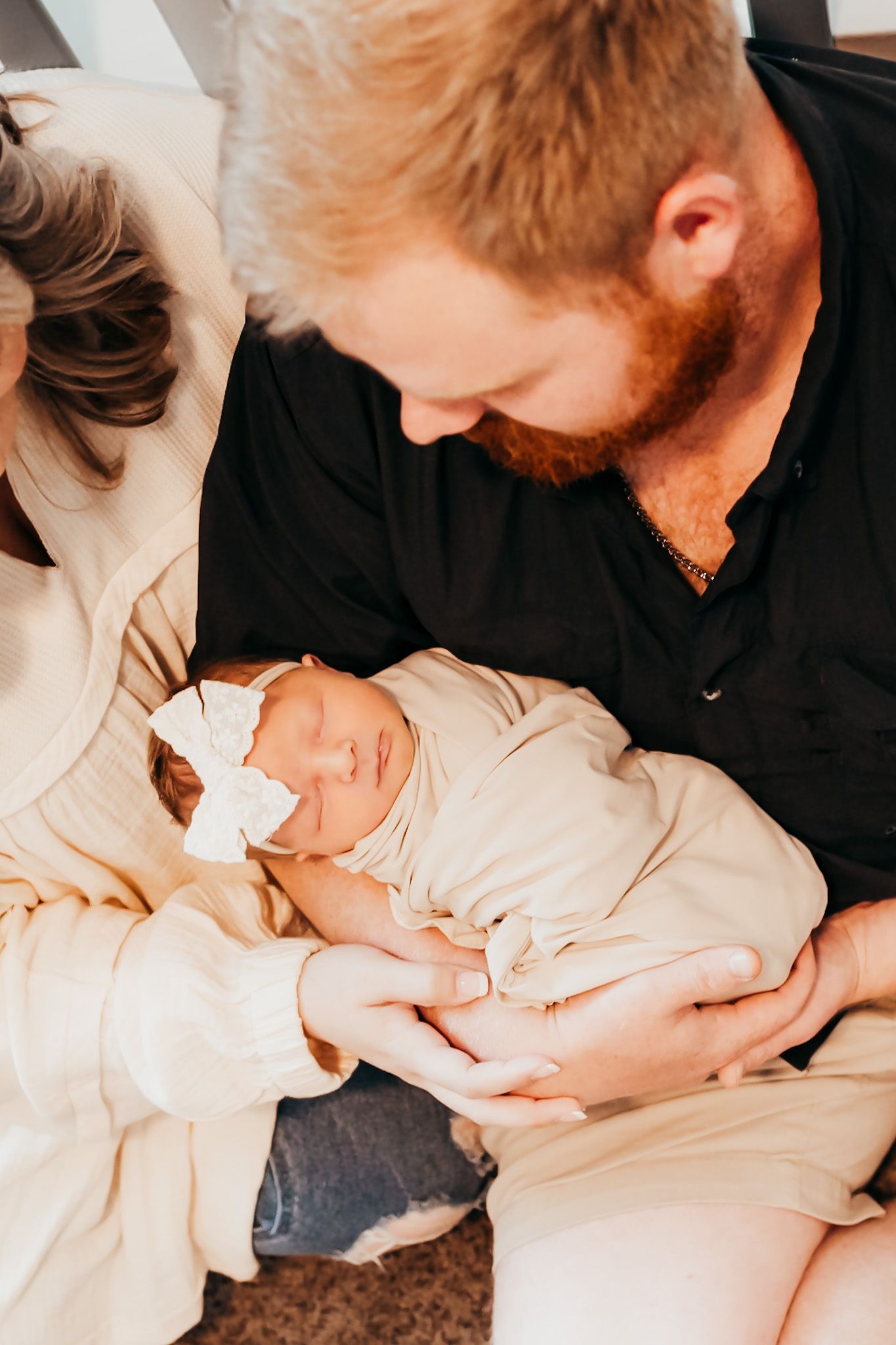 mom and dad holding up their newborn baby swaddled with a bow