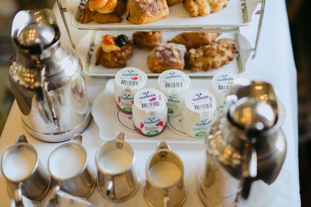 Elegant tea service display with pastries on tiered stand and white ceramic milk jugs arranged on table.
