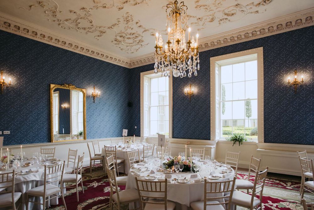 Elegant dining room with navy blue wallpaper, crystal chandelier, and white wainscoting in a historic mansion.