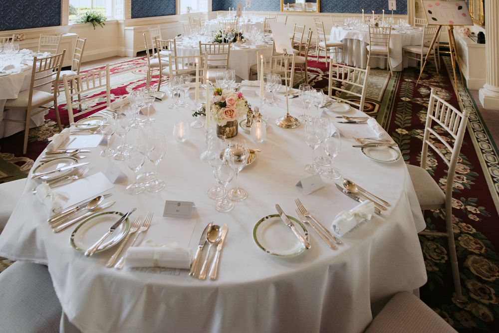 An elegant wedding reception table set with white linens, gold chiavari chairs, and delicate floral centerpieces.