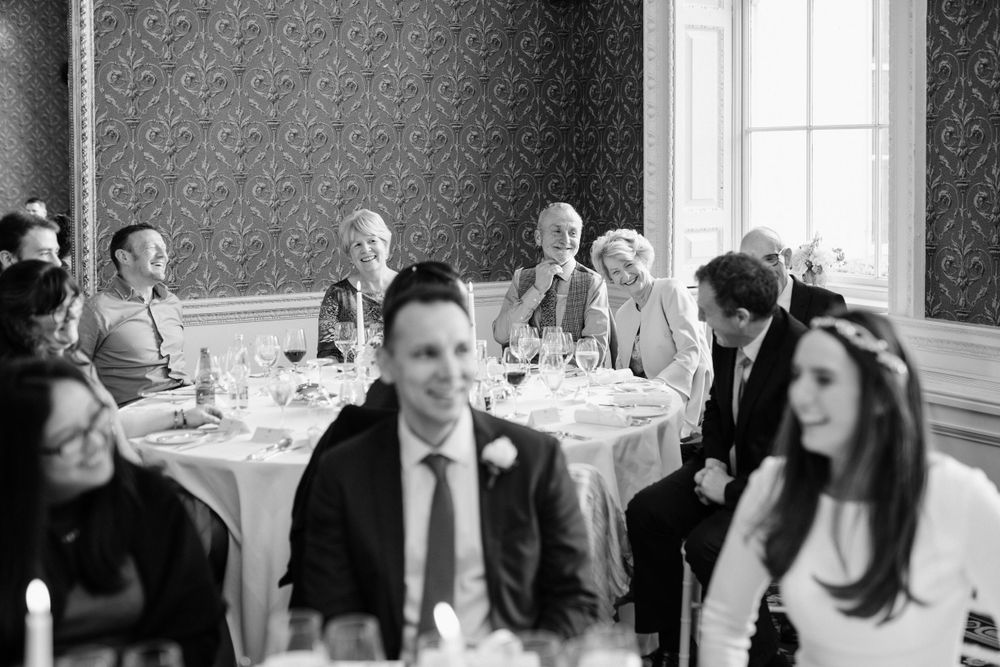 Wedding guests enjoy conversation at elegant dining tables in a formal room with ornate wallpaper during reception.