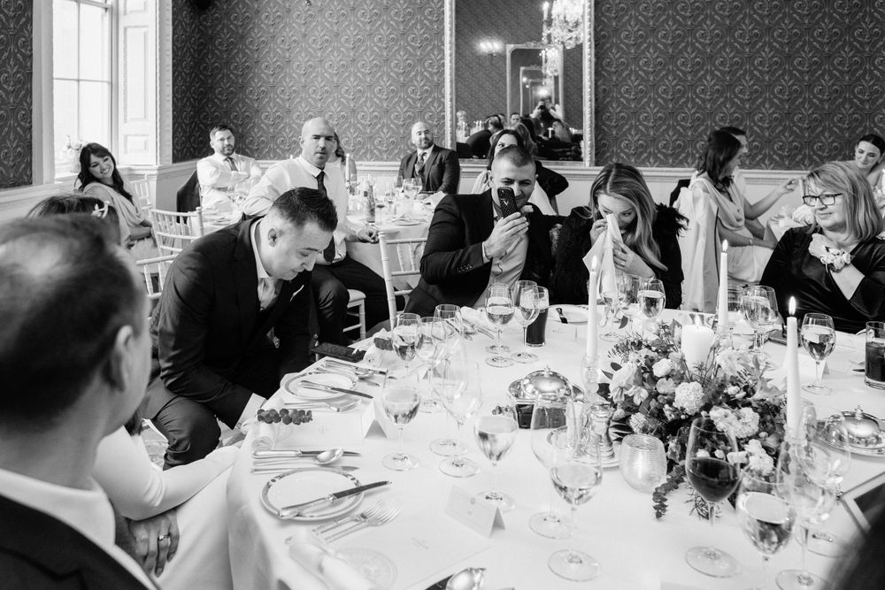 A black and white photograph captures guests dining and socializing at an elegant formal dinner reception.