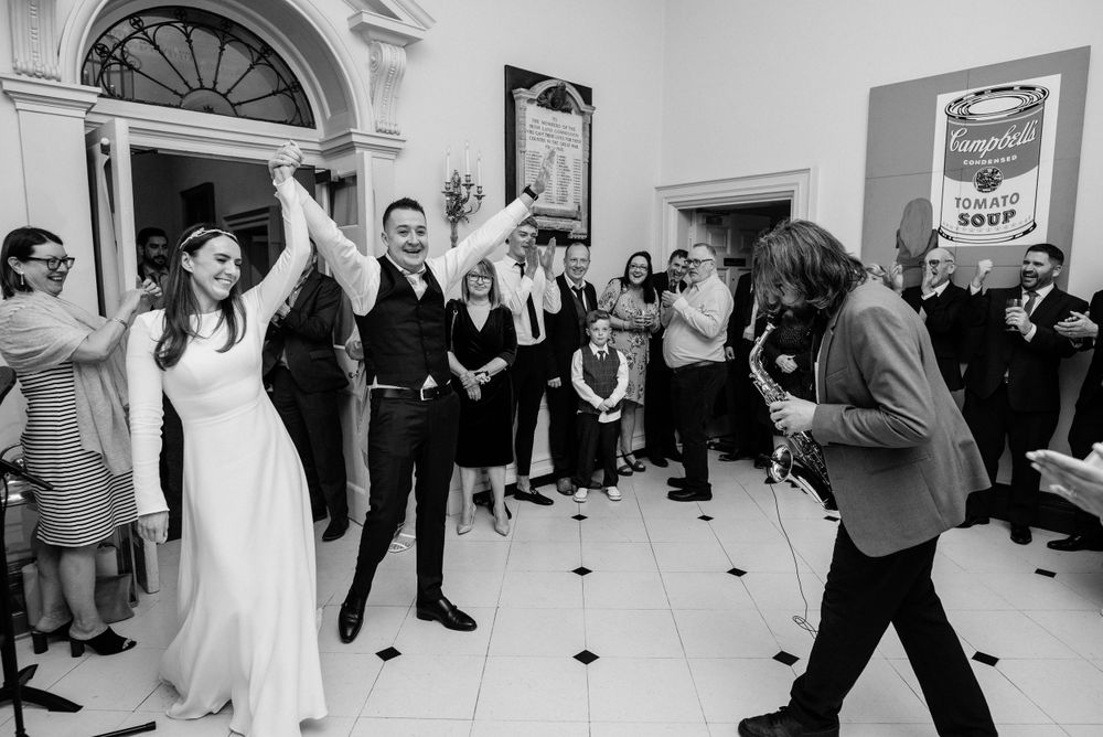 A joyful celebration at an indoor wedding reception with people dancing on a black and white checkered floor.